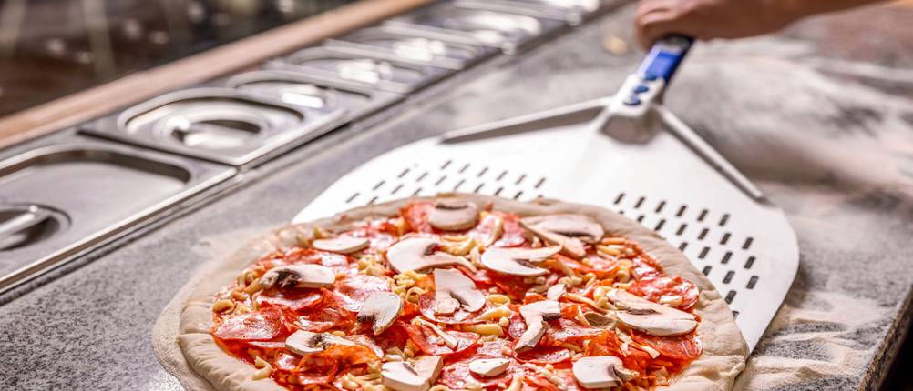 Eine Person schiebt eine Pizza auf eine perforierte Pizzaschaufel aus Metall.