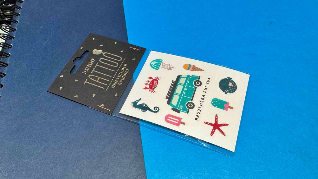 Eine Verpackung mit temporären Tattoos im Test liegt auf einer blauen Oberfläche.