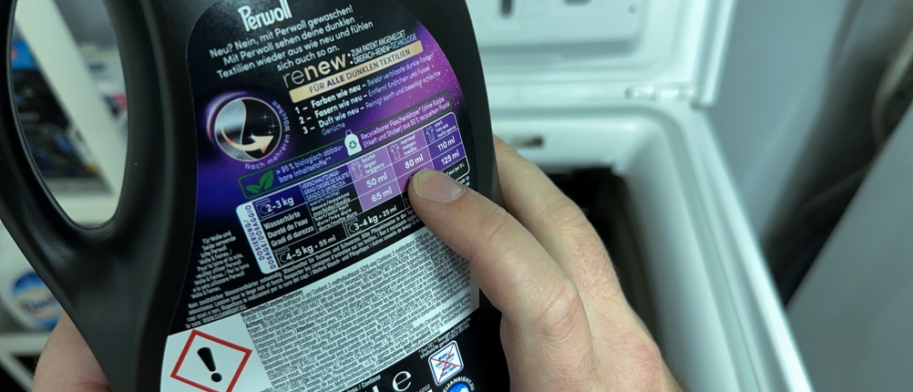 Eine Dosierungsanleitung auf der Rückseite der Flasche des Waschmittels für schwarze Wäsche von Coral wird betrachtet.