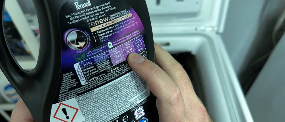 Eine Dosierungsanleitung auf der Rückseite der Flasche des Waschmittels für schwarze Wäsche von Coral wird betrachtet.