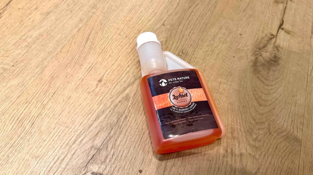 Im Test: Lachsöl für Hunde in einer Kunststoffflasche mit Dosierkappe liegt auf einer Holzoberfläche.