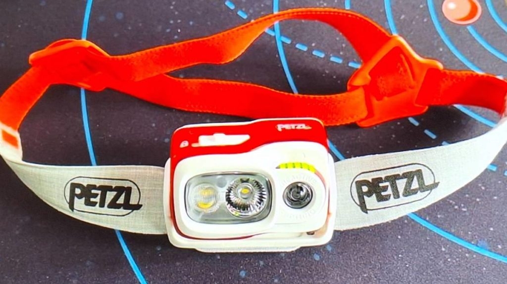 Ansicht einer weiß-roten, getesteten Stirnlampe von Petzl auf einem blau-grauen Kinderspielteppich.