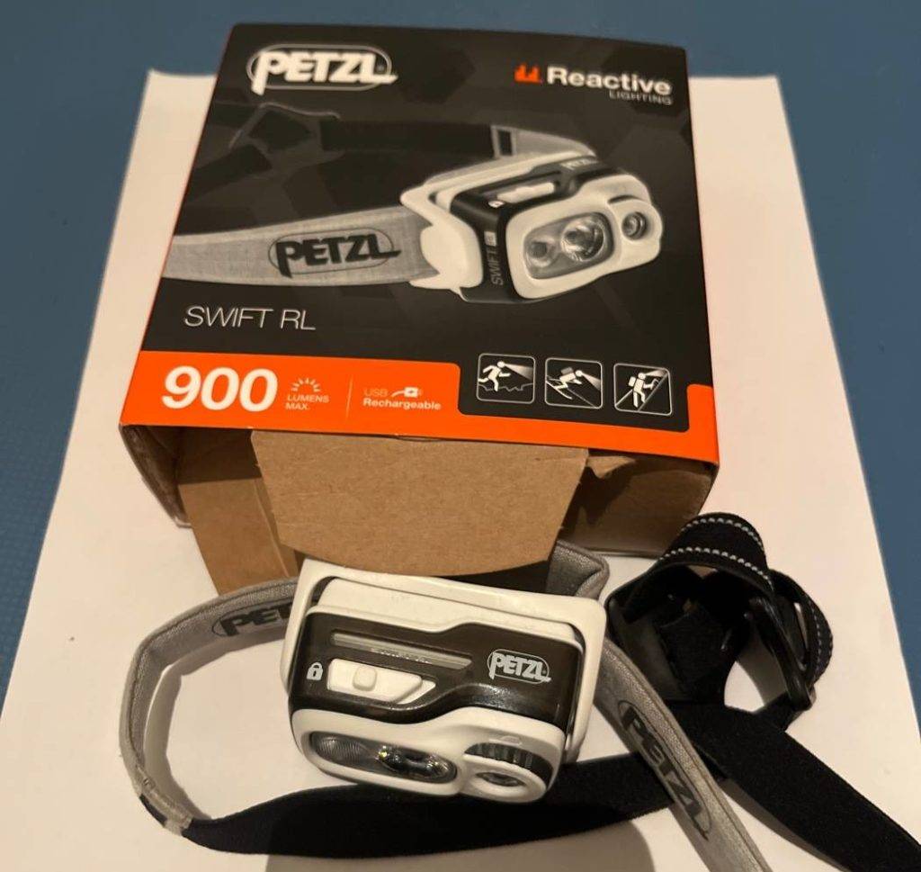 Seitenansicht einer weiß-schwarzen, getesteten Stirnlampe von Petzl mit max. 900 Lumen befindet sich außerhalb der Originalverpackung.