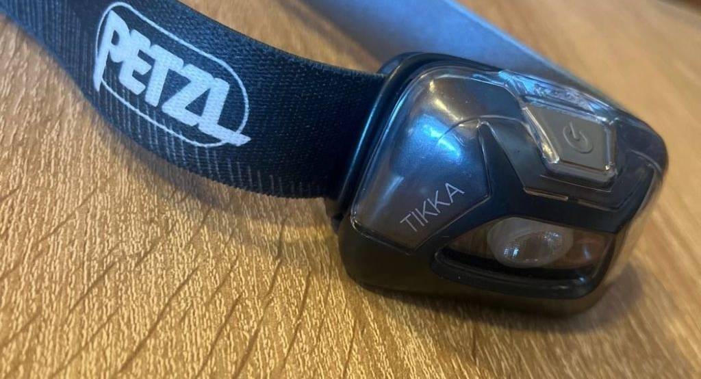 Schwarze, getestete Stirnlampe von Petzl befindet sich auf einer Holzfläche.