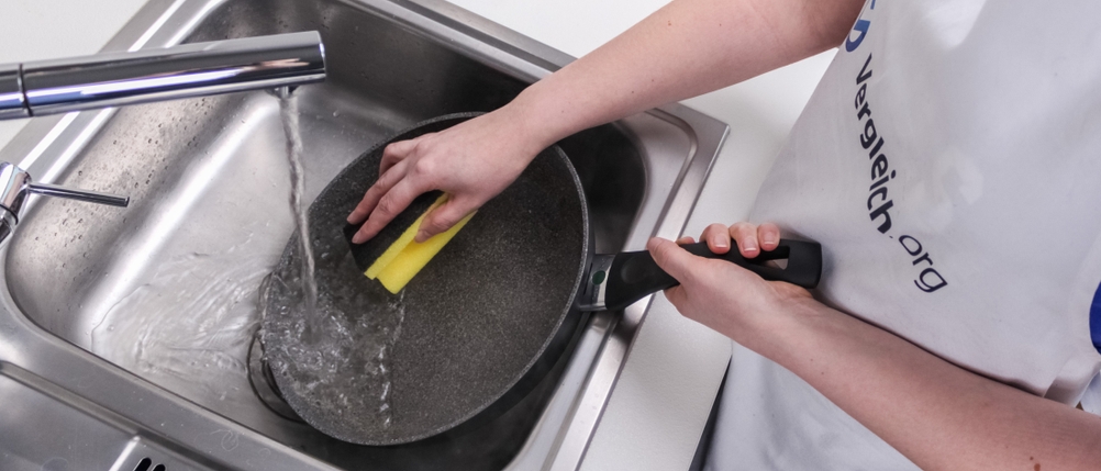 Pfannen-Test: Eine Person reinigt eine Pfanne mit einem Schwamm unter dem Wasserhahn.