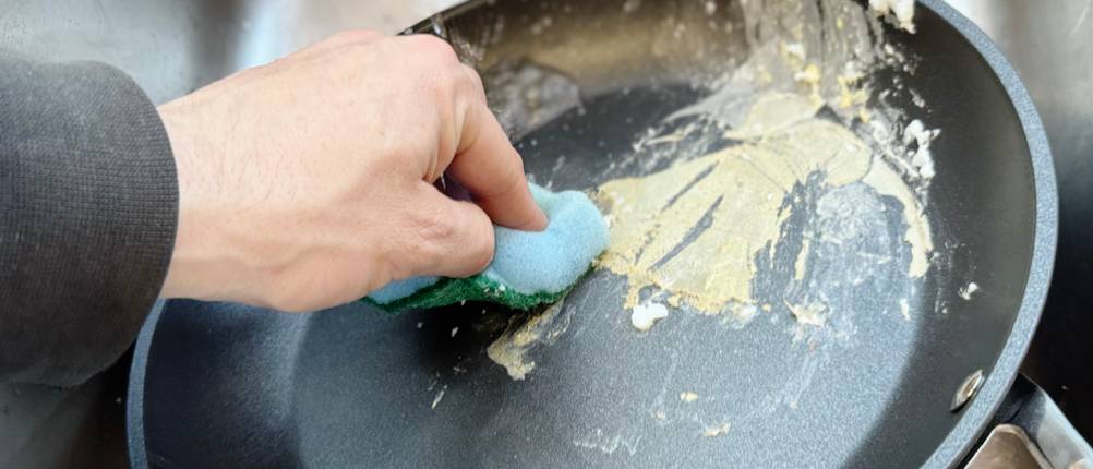 Eine Person reinigt mit einem Küchenschwamm die getestete Pfanne von Le Creuset.