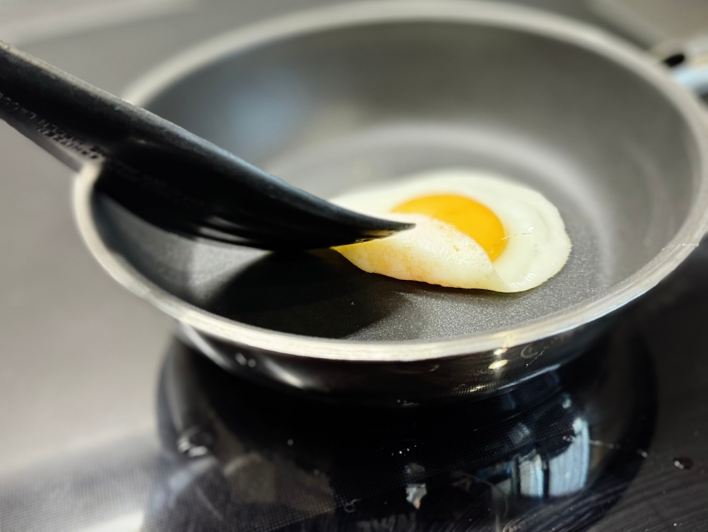 Eine Person hebt mit einem Pfannenwender ein Spiegelei in einer Pfanne des getesteten Pfannensets von Rösle an.