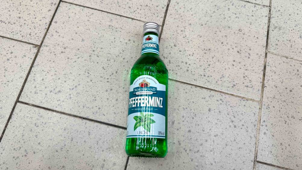 Auf dem Fließenboden liegt eine Flasche des Pfefferminzlikörs im Test.