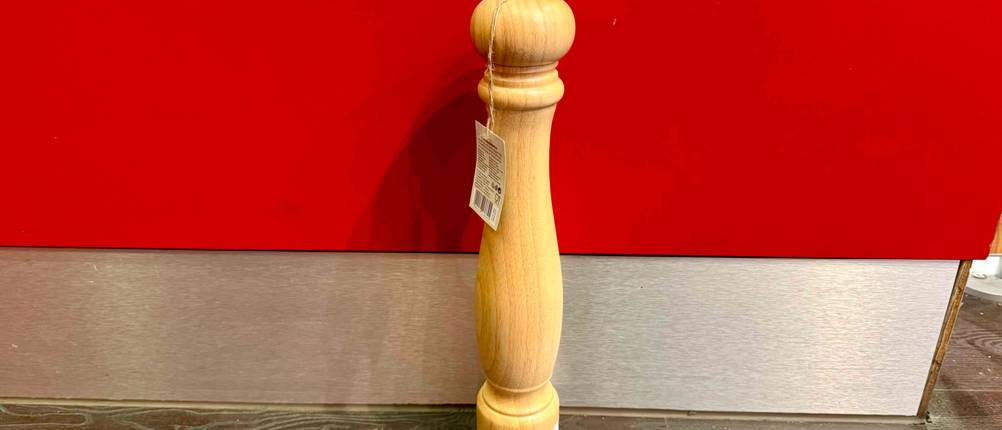 Vor einer roten Wand steht eine getestete Pfeffermühle groß auf dem Boden.