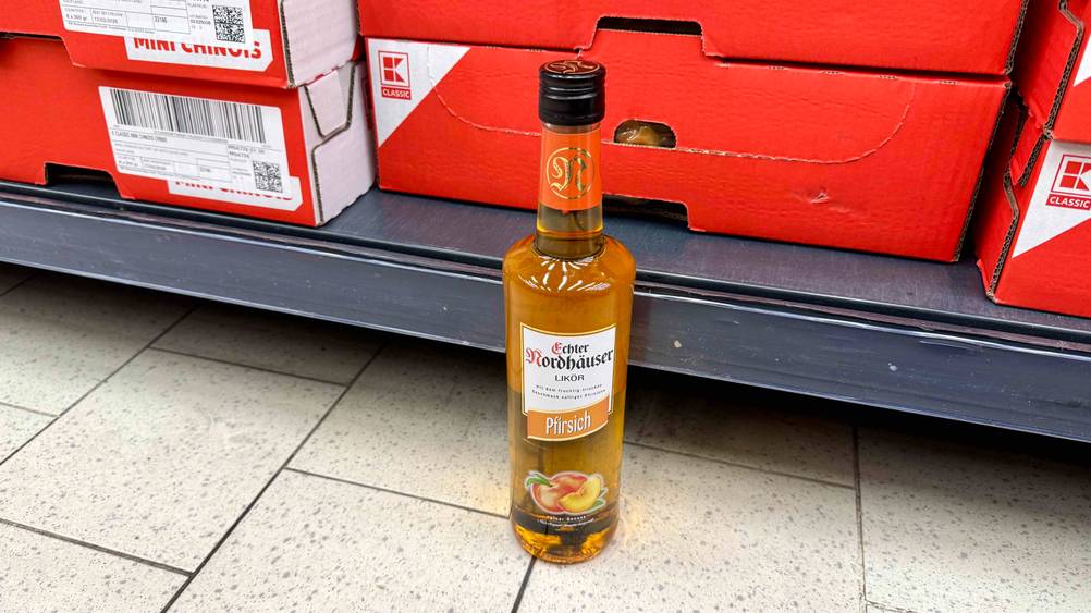 Vor einem Regal mit roten Kartons steht eine Flasche des getesteten Pfirsichlikörs.
