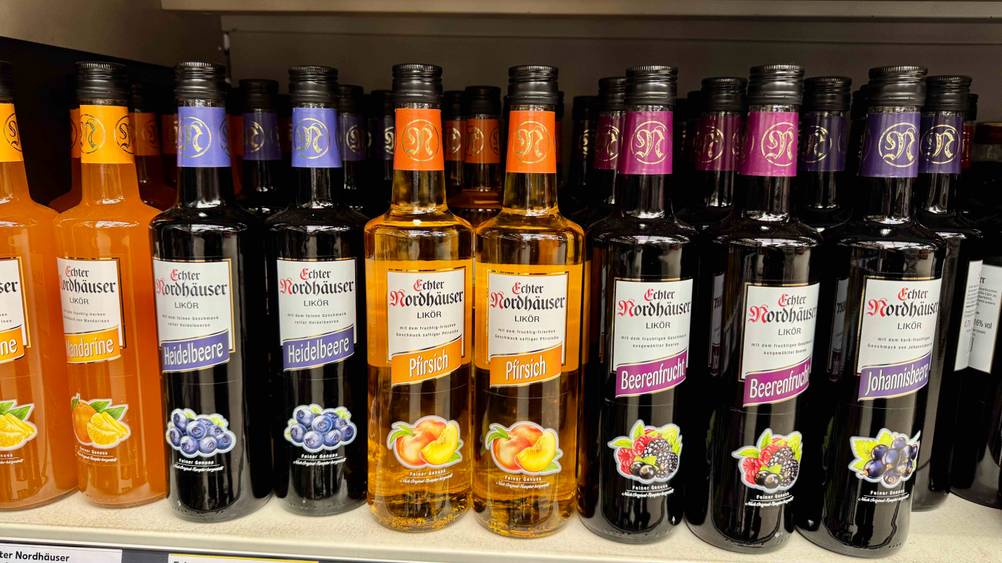 Mehrere Flaschen des Pfirsichlikör im Test in einem Verkaufsregal neben anderen Produkten.