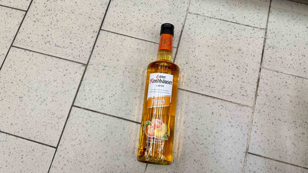 Pfirsichlikör im Test: Eine Flasche von oben auf einem Fließenboden liegend.