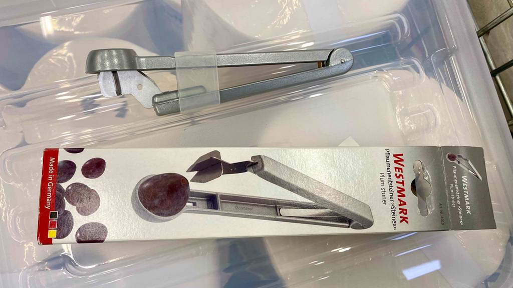 Ein getesteter Pflaumenentsteiner aus Edelstahl befindet sich neben der Verpackung. 