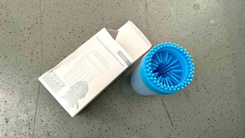 Ein getesteter Pfotenreiniger steht neben seiner Originalverpackung auf einer grauen Fläche.
