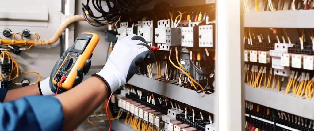 Phasenkoppler im Test: Eine Elektro-Fachkraft mit Handschuhen und Prüfgerät vor einem Netzwerkkasten