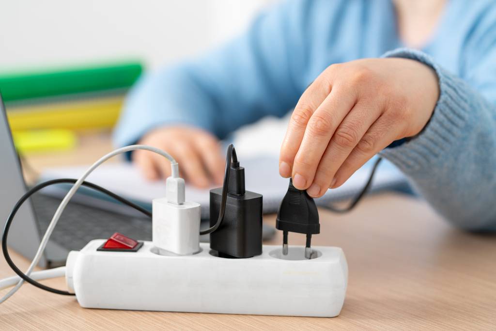 Phasenkoppler im Test: Eine Person in hellblauem Pullover steckt einen Stecker in eine Mehrfachsteckdose, die auf einem Schreibtisch vor einem Laptop steht.