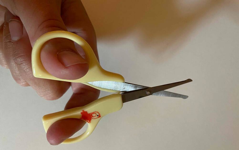 Eine erwachsene Hand hält eine getestete Baby-Nagelschere.