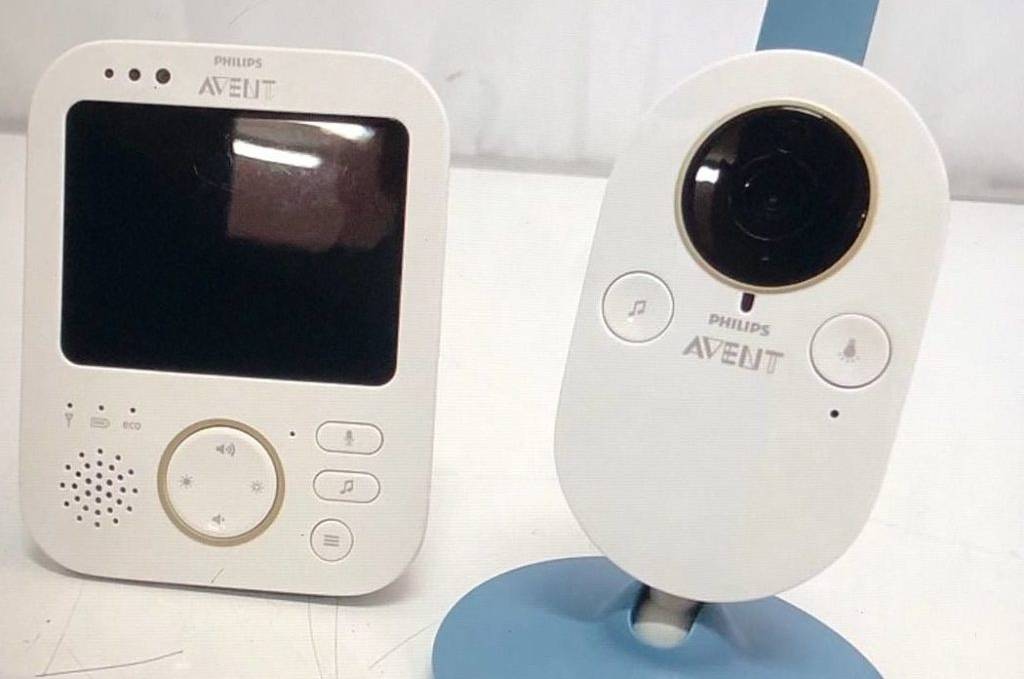 Getestete Philips-Avent-Baby-Kamera im blau-weißen Design steht neben dem dazugehörigen Bildschirm-Element und der Bedienungsanleitung auf einer weißen Fläche.