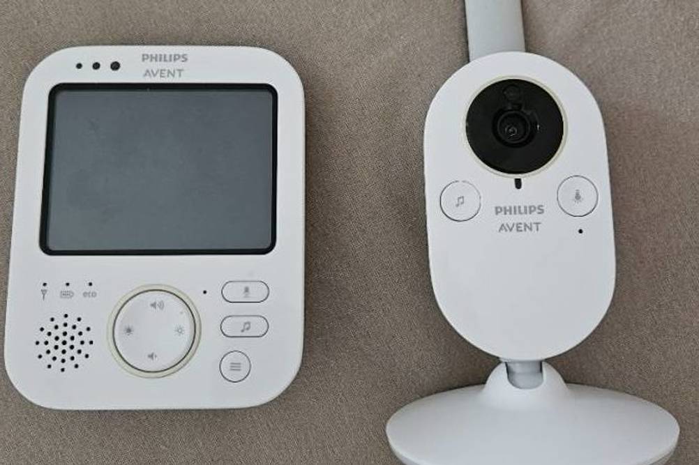 Baby-Kamera-Test: Gesamtansicht der Kamera und des Wiedergabe-Bildschirms im weißen Design, die nebeneinander kabellos auf einem grauen Stoff liegen.