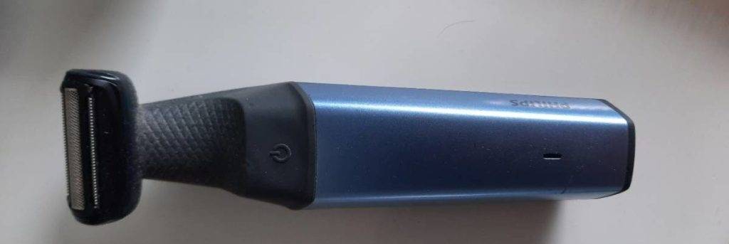 Schwarz-hellblauer, elektrischer, getesteter Philips Körperrasierer befindet sich mit Fokus auf den Schneid-Aufsatz ohne direkte Klingen und den Einschaltknopf auf weißem Untergrund.