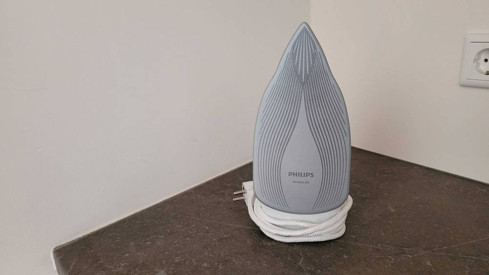 Ein getestetes Philips Bügeleisen steht mit zusammengerolltem Kabel mit der Unterseite nach vorn auf einer dunklen Fläche.