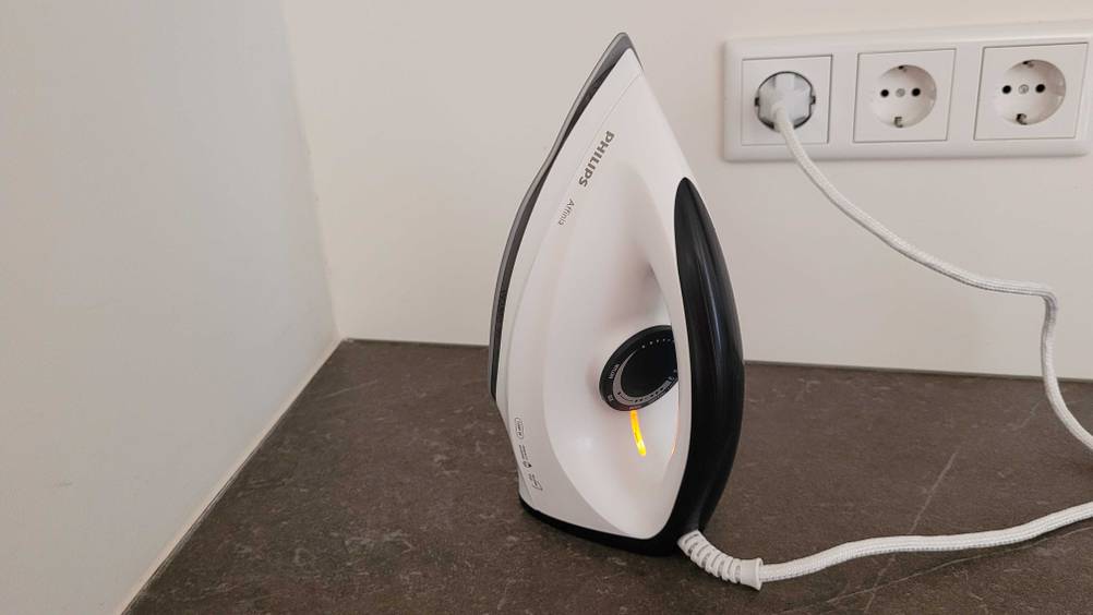 Ein Philips Bügeleisen im Test ist an den Strom angesteckt und steht hochkant auf einer dunklen Fläche.