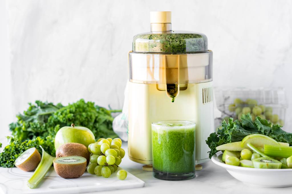 Philips-Entsafter-Test: In einem Entsafter wird grüner Saft entsaftet. Um das Gerät herum liegen Gemüse und Obst. 