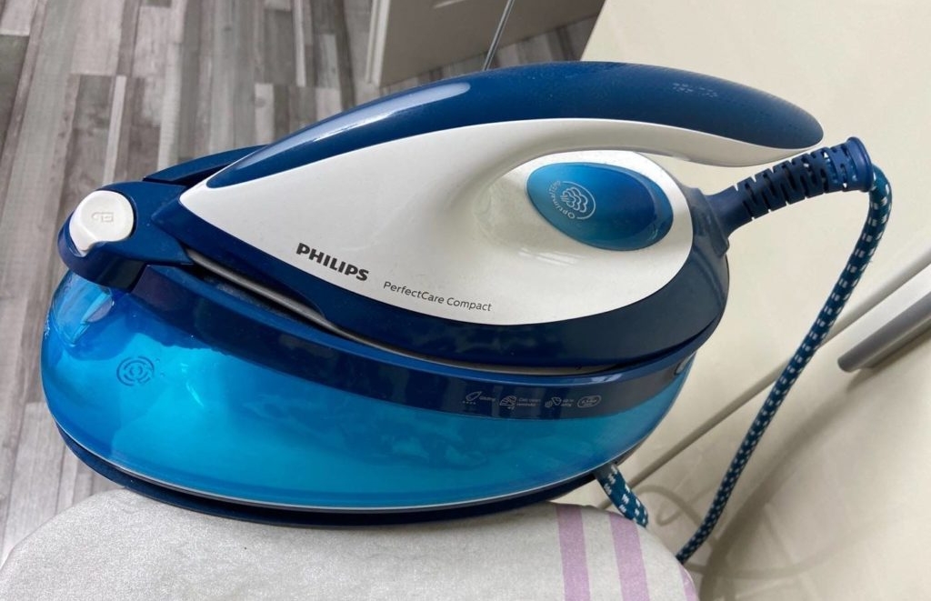 Dampfbügelstation im Test: Philips PerfectCare Compact im weiß-blauen Design steht auf einer hellen Bügelbrettablage.