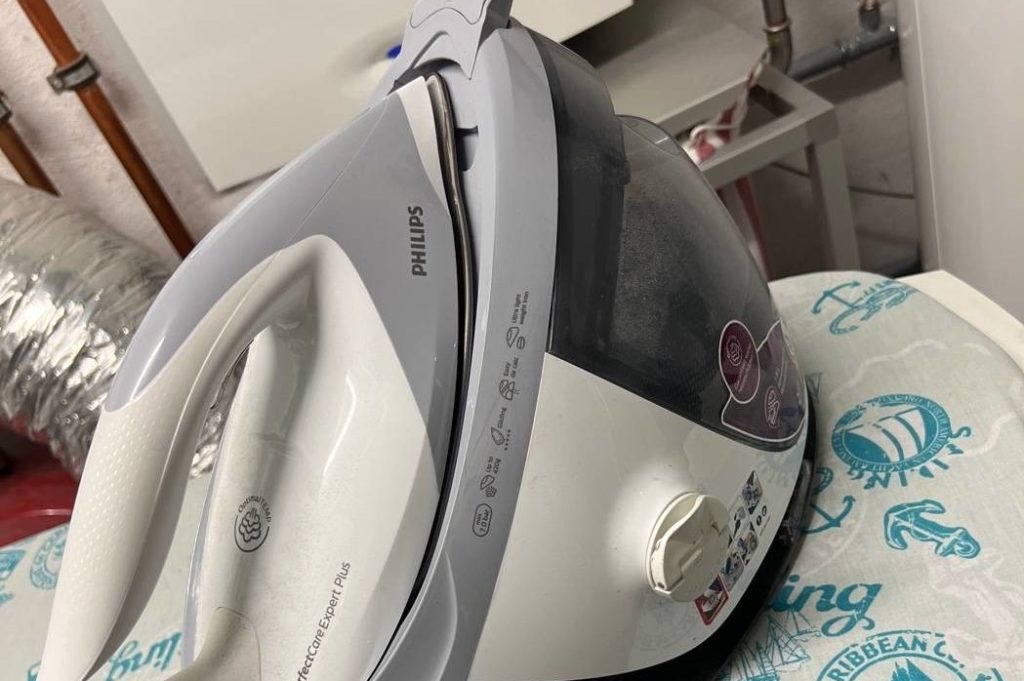 Dampfbügelstation-Test: Das grau-cremefarbige Modell PerfectCare Expert Plus von Philips befindet sich auf einer gemusterten Bügelbrettablage in einem Haushaltsraum.