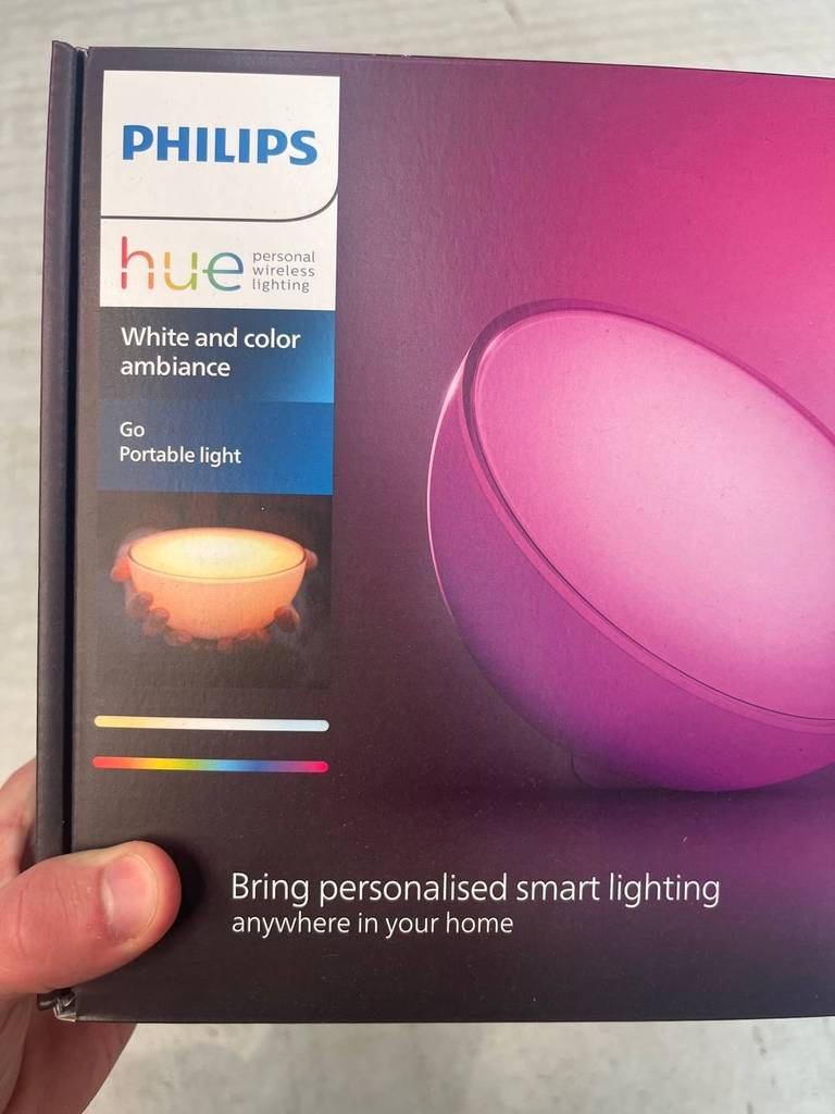 Tageslichtlampen-Test: eine Hand hält eine violett-rosa Verpackung einer Philips Hue White & Col. Amb. LED Tischleuchte Go.