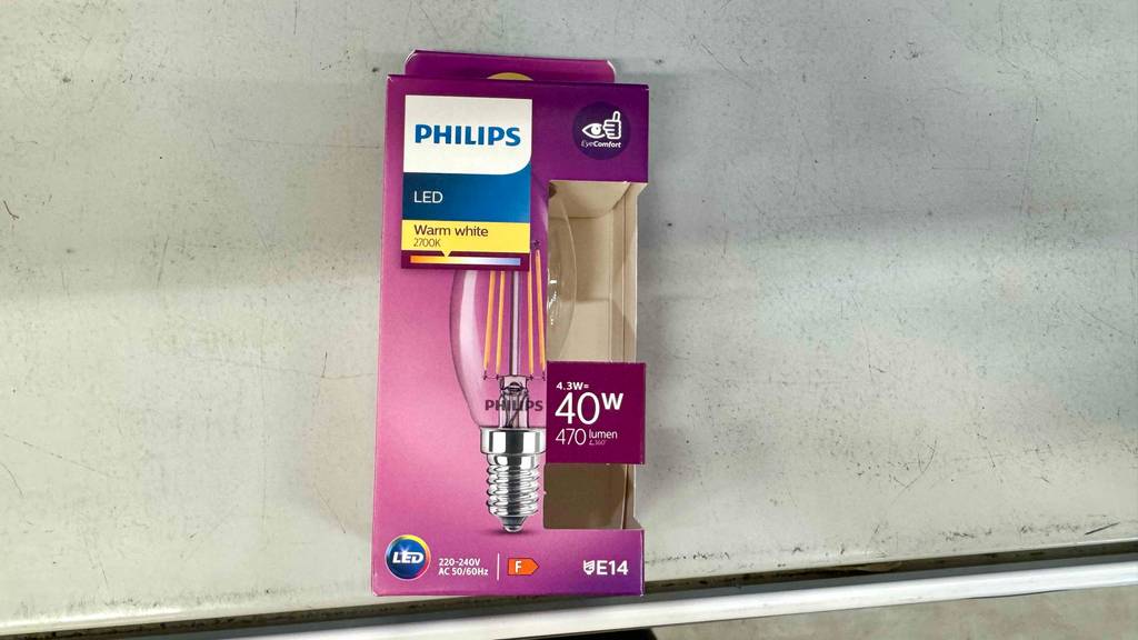 Ein pinke Verpackung mit einer getesteten LED-Lampe E14 steht auf einem weißen Regal.