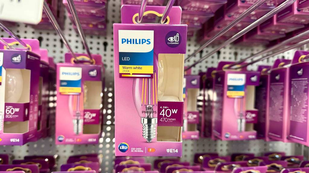 Ein pinke Verpackung mit einer LED-Lampe E14 im Test hängt vor weiteren Lampenprodukten der Marke Philips an einem Verkaufsstand.