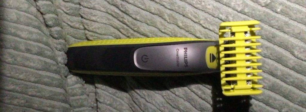 Nahaufnahme von einem schwarz-gelben Philips OneBlade Bartschneider im Test inklusive eines gelben Hautschutzaufsatzes auf einer grauen Decke.