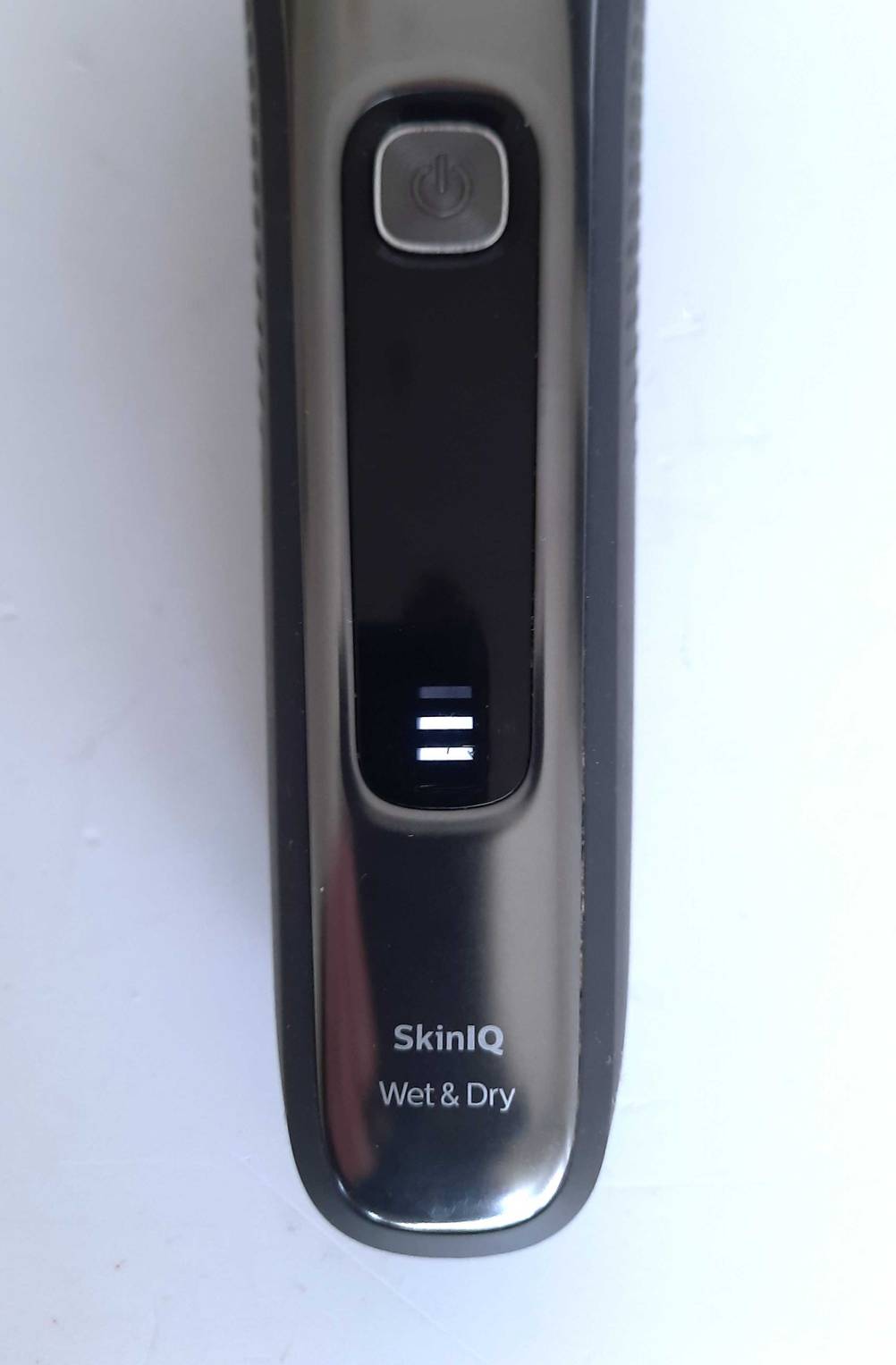 Nahaufnahme des Power-Knopfes und der Akkustandanzeige eines getesteten Philips-Rasierers auf einer hellen Fläche.