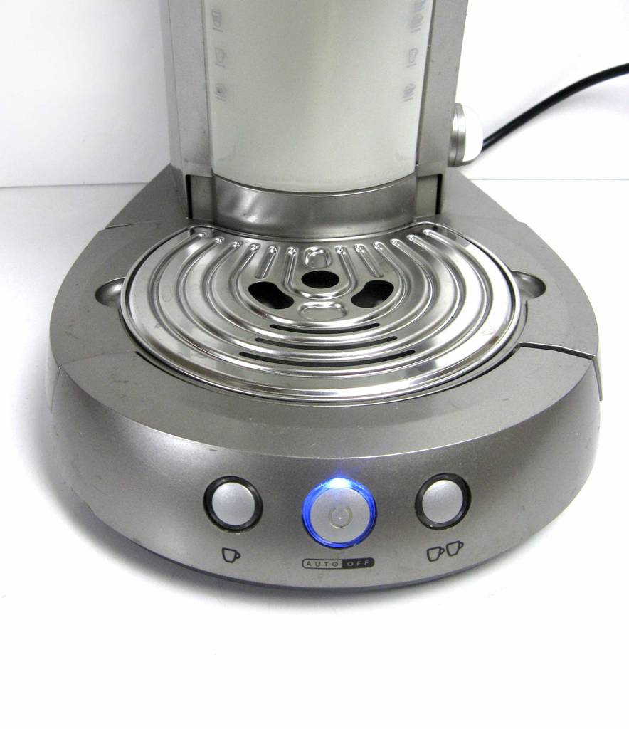Ansicht der blau leuchtenden Einschalttaste im Bodenbereich der getesteten Kaffeemaschine für Singles in Silbergrau.