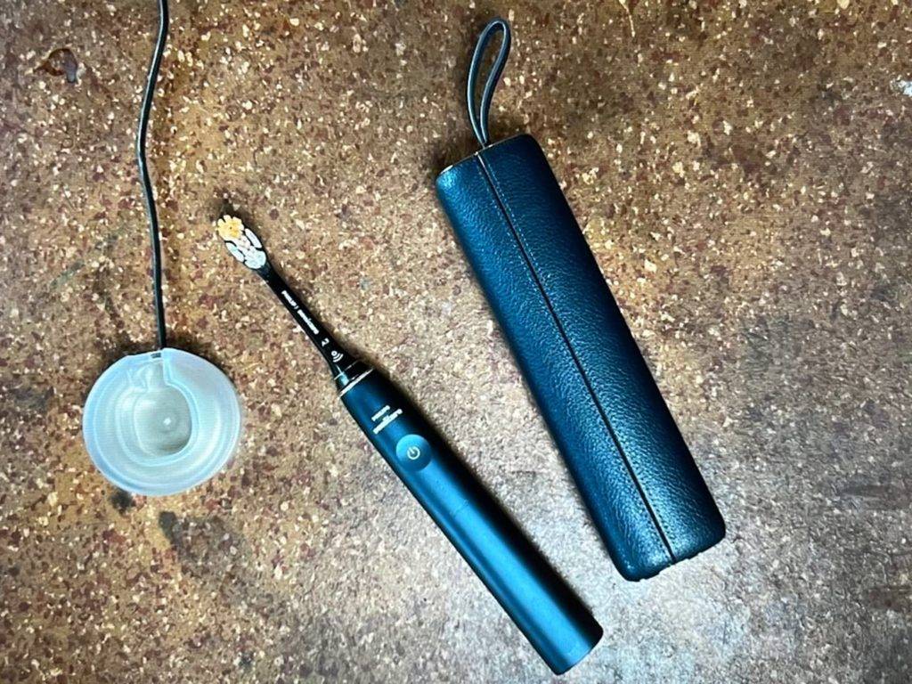 Im Test: Schallzahnbürste von Philips in schwarzem Design liegt neben ihrer Ladestation und einem dunklen Aufbewahrungsetui auf braunem Untergrund.