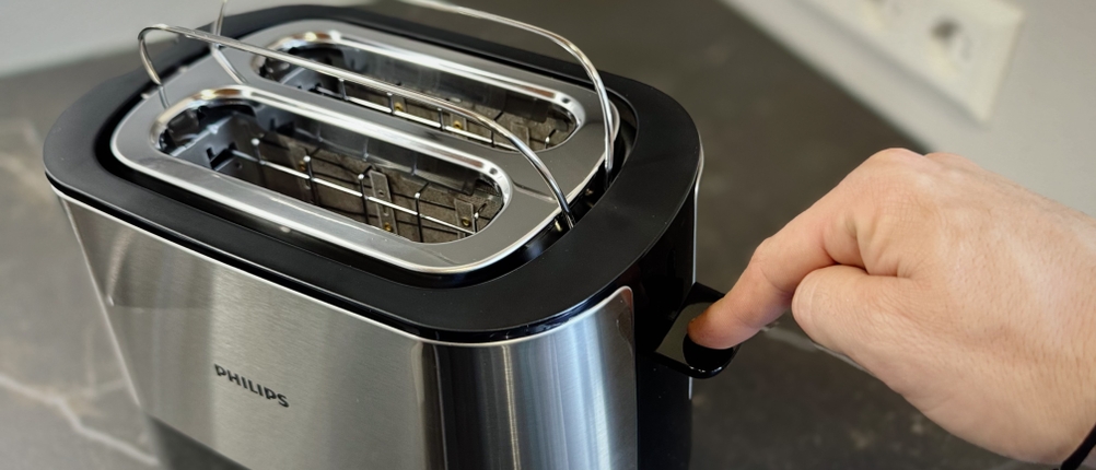 Eine Person drückt auf den Hebel des getesteten Toasters und zwei Metallbügel klappen nach oben.