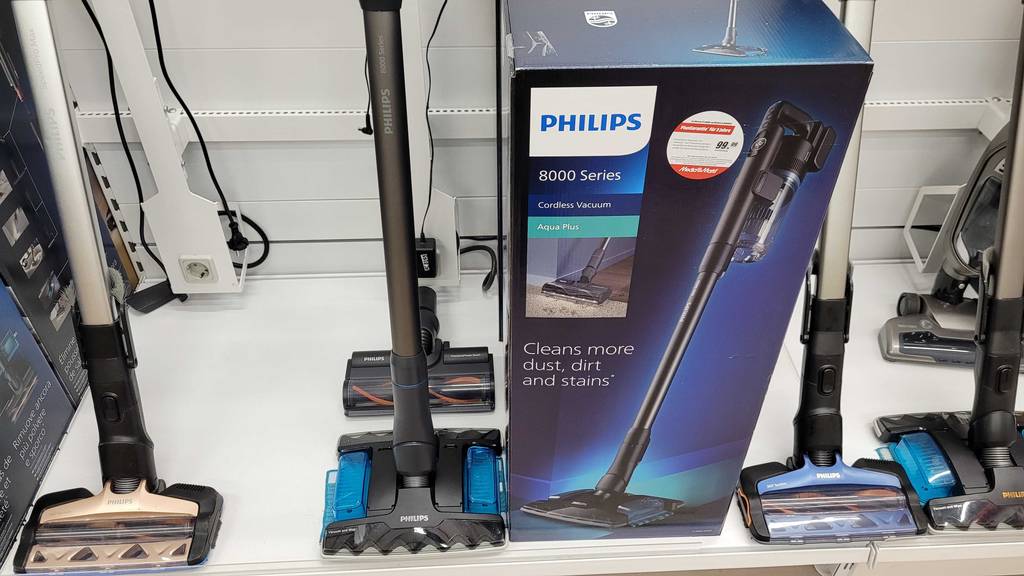 Philips-Akku-Staubsauger-Test: kabelloses schwarzes Modell der 8000 Series steht neben seiner blauen Originalverpackung in einem Verkaufsbereich neben anderen Staubsaugern.