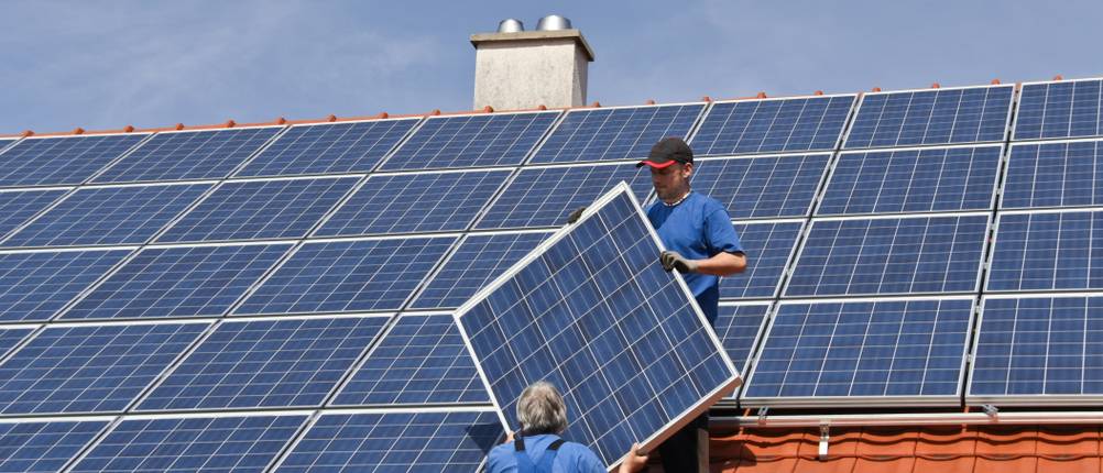 Zwei Handwerker in Sicherheitskleidung montieren Solarmodule auf einem Hausdach.