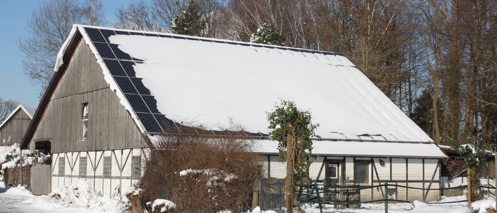 Eine moderne Solaranlage auf einer Scheune ist komplett von Schnee bedeckt.