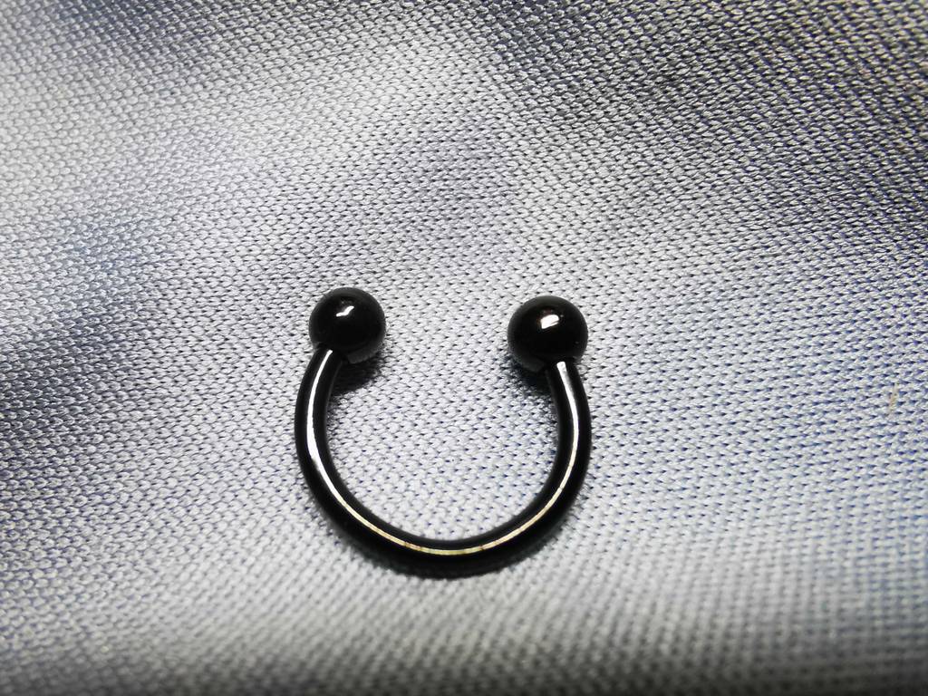 Ein schwarzes Piercing in Hufeisenform liegt getestet auf einer hellen Fläche.