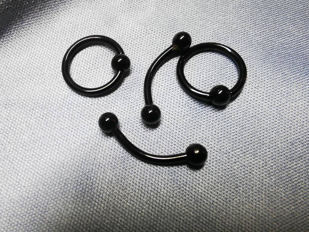 Getestet: Mehrere schwarze Piercinge liegen als Gesicht auf einem Tuch.