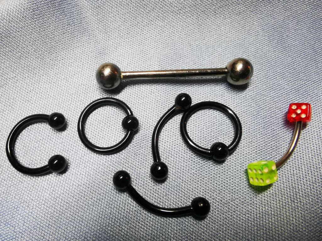 Mehrere Piercinge in unterschiedlichen Formen liegen zum testen auf einer hellen Fläche.