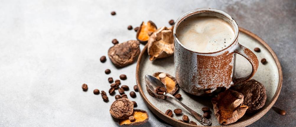 Pilzkaffee in einer Tasse mit dekorativen Pilzen und Kaffeebohnen rundherum.