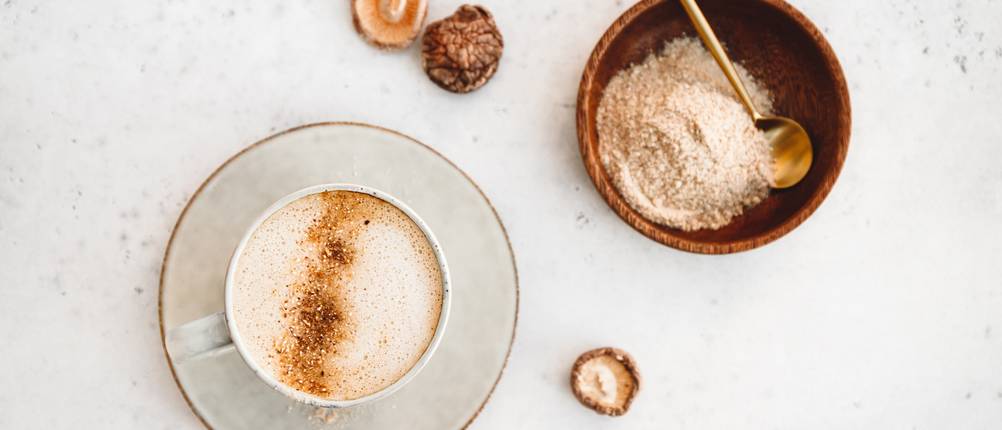 Kaffee steht neben einer Schale mit Vitalpilz-Pulver auf der Anrichte.