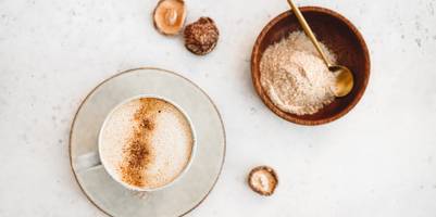 Kaffee steht neben einer Schale mit Vitalpilz-Pulver auf der Anrichte.