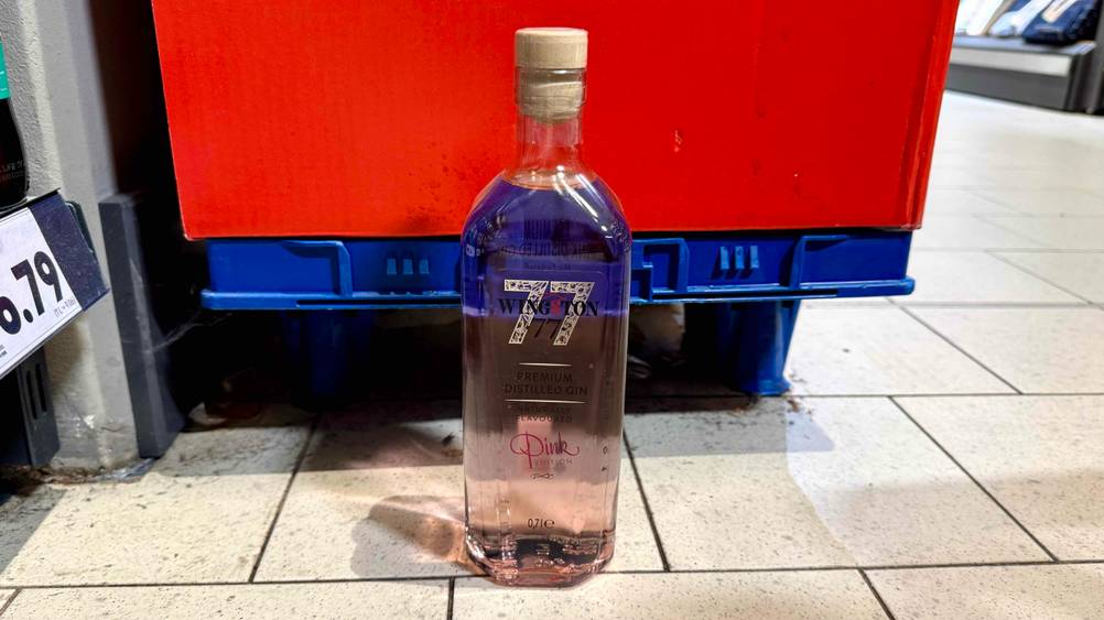 Vor einer Plastikpalette steht eine Flasche des getesteten Pink Gins auf dem. Boden.