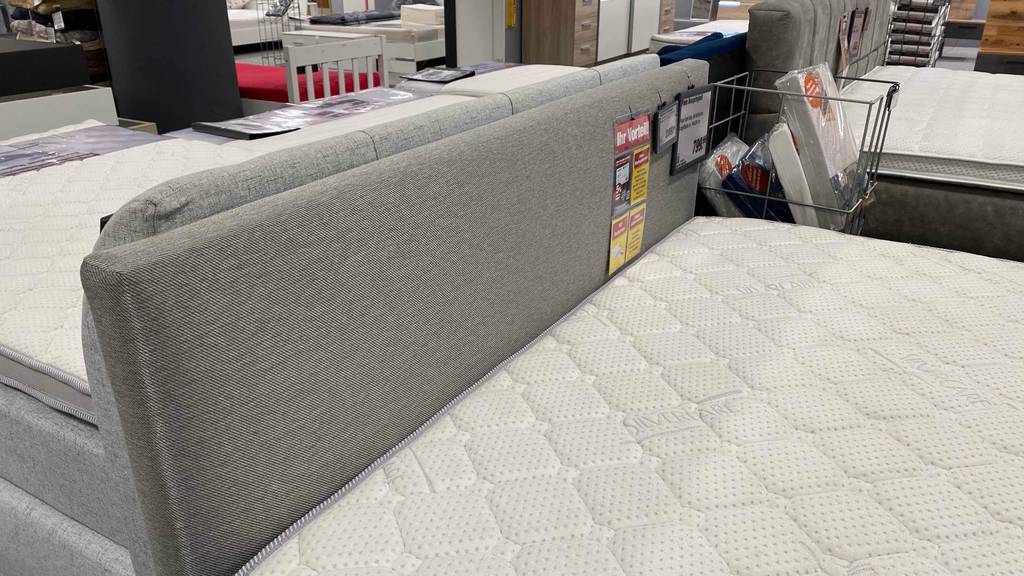 Im Test: Boxspringbett 140 x 200 cm in hellgrauem Design inklusive Kopfteil sowie Topper in einem Geschäftsbereich.