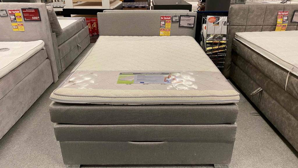 Im Test: mit beigefarbenem Stoff verkleidetes Boxspringbett 140 x 200 cm inklusive Topper in einem Geschäftsbereich.