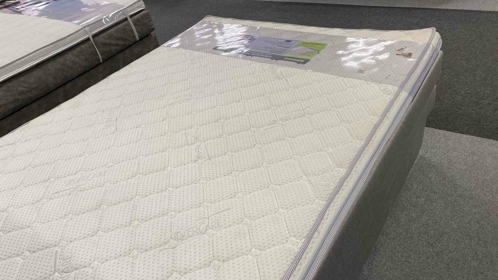 Im Test: Boxspringbett 140 x 200 cm, mit beigefarbenem Stoff verkleidet, inklusive gestepptem Topper in einem Ausstellungsbereich.